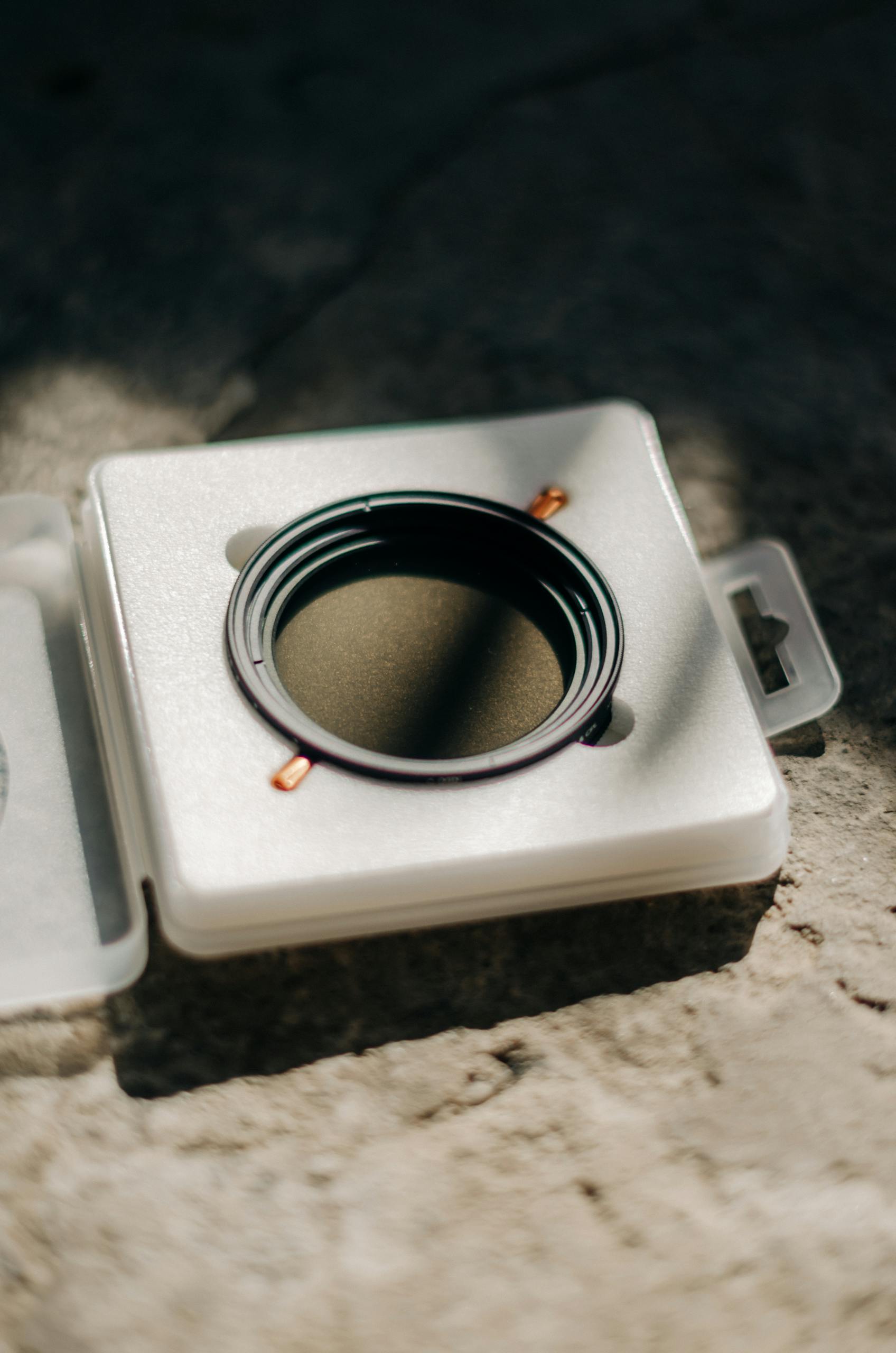 A camera lens filter sits securely in a lightweight protective box. Ideal photography gear.